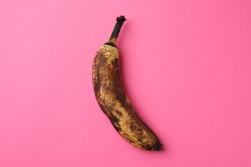 Overripe banana with dark spots on pink background, top view