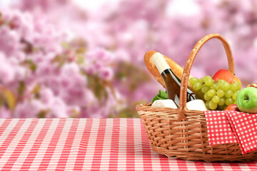 Picnic basket with foods and wine on table in nature. Space for text