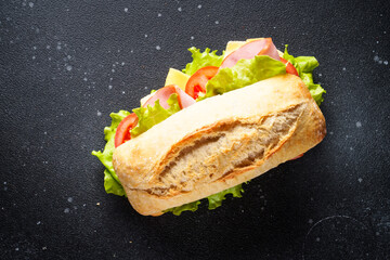 Ciabatta sandwich with lettuce, cheese, tomatoes and ham on black background. Fast food, snack or...