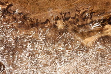 A small run-off stream of water runs beneath the frozen surface on the beach sand at Harrington Beach State Park, Belgium, Wisconsin in mid-January during a rare sunny, warm morning