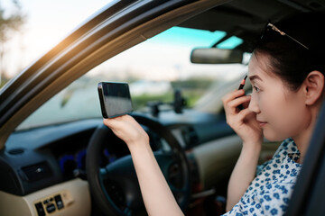 A young woman paints her eyebrows while driving