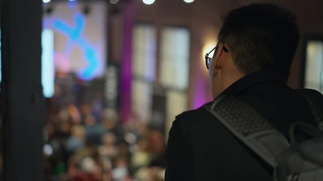 Young entrepreneur with backpack stands amidst a startup event. observing a networking opportunity, relevant for young entrepreneurs, startup culture, business incubators