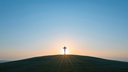 Obraz premium Silhouette of a cross on a hilltop with the sun rising behind it. The sky is a clear blue, and the ground is covered in grass.