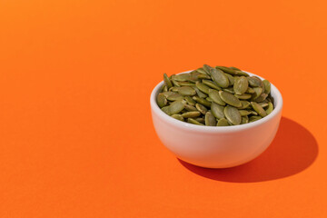 Fresh Pumpkin Seeds in White Bowl on Vibrant Orange Background - Minimalist Healthy Snack Concept