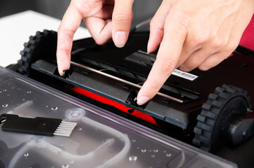Close-up of a young Caucasian woman's hands servicing the brush compartment of a robot vacuum cleaner. Automated home cleaning systems