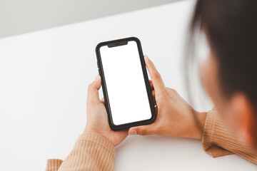 Woman in a yellow sweater uses smartphone with blank screen while working at her desk.