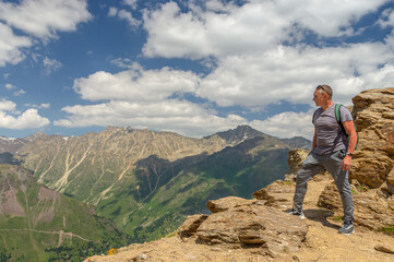 A man looks at the high snow-capped mountains. The conquest of the mountains.  The rocks are located high in the mountains. The nature of the highlands.