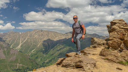 A man looks at the high snow-capped mountains. The conquest of the mountains.  The rocks are located high in the mountains. The nature of the highlands.
