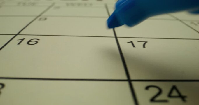 A person crosses out a number in the schedule table with a blue marker. Close-up of the marker, an unrecognizable person