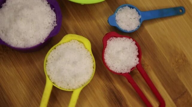 Small crystals of white sea salt in colorful measurement spoons rotate video. 1 tbs measurement. Table spoon salt concept.
