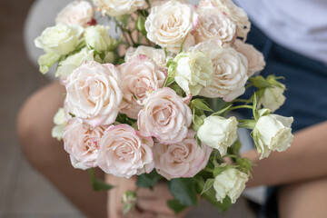 A bouquet of beautiful white rose flowers in the hands of a man sitting indoors, closeup. Romance, present, love concept