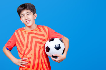 Kid holding soccer ball under his arm. Isolated on blue background. Sports.