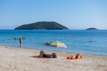 People relaxing on a sandy beach with a view of a distant island on a sunny day