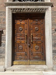 Old facade wall of a building with an entrance door. Double wooden doors. Church entrance with marble steps leading to a sunny street in Athens, Greece.
