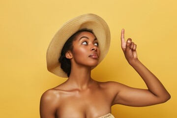 Shirtless fit black woman with thoughtful expression in a straw hat, pointing upwards Isolated color background