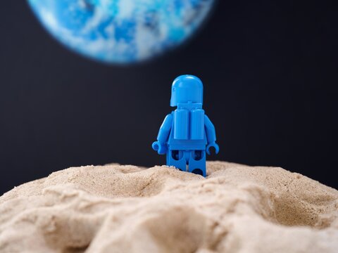 Tambov, Russian Federation - July 28, 2024 Lego astronaut minifigure standing on sand on a planet and looking at another blue planet. Back view.
