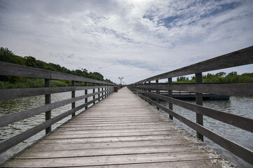 Fototapeta premium Wooden pathway through pond under dramatic cloudy sky
