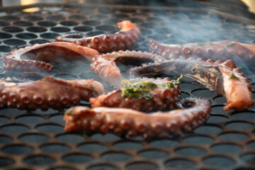 octopus tentacles grilling on hot coals with smoke close-up