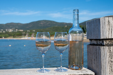 Bottle and glass of cold rose wine from Provence and wooden yacht boota pier on white sandy beach Plage de Pampelonne near Saint-Tropez, summer vacation in France