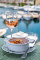 Homemade tasty fish or bisque soup with croutons served with glass of cold rose wine and view on yacht boats and houses of Port Grimaud, French Riviera, France. Food of Provence