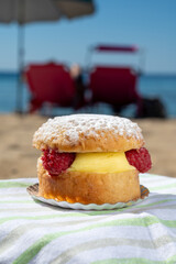 Lunch on sandy beach in Saint-Tropez with cake Tarte tropezienne filled brioche with cream and fresh red berries, summer vacation on French riviera, France