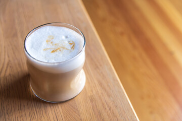 Close-up side view of drinking glass with latte macchiato standing on wooden table in cafe or restaurant. Copy space. Soft focus. Coffee beverages theme.