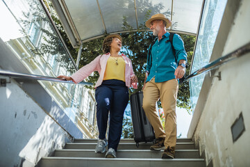 Mature married couple walking down the stairs, entering metro with luggage.