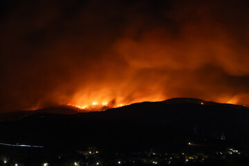 Reflections of a massive wildfire blaze in the night over the hills
