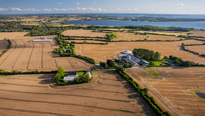 Rural landscape with cereal fields, windmill, pig farms, silos and farmhouses in the Danish countryside near Nybøl Nor lagoon. Hedging landscape with agricultural fields and farms. © snapshotfreddy