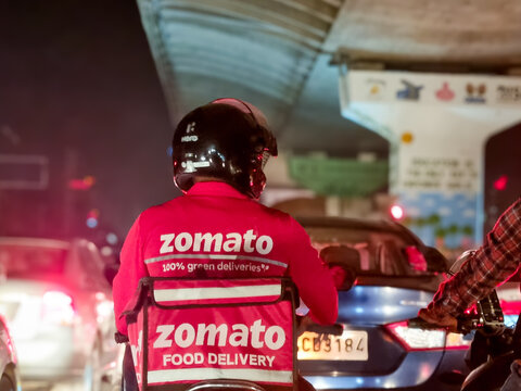 Delivery boy rider from food delivery app Zomato stuck in traffic on a rainy night showing the busy lifestyle