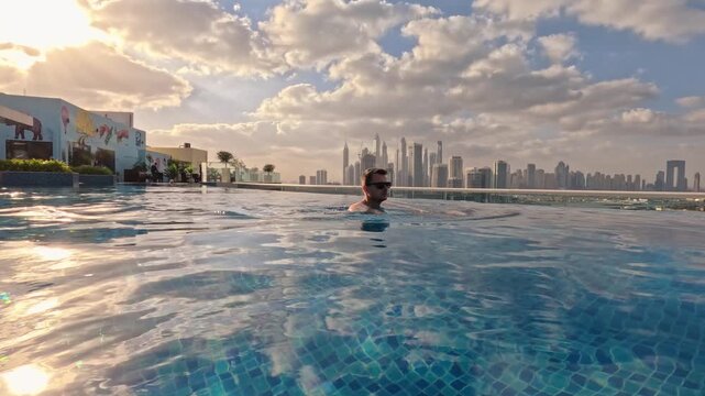 Dubai lifestyle video of travel man  swimming in an infinity pool at sunrise, with the Dubai Marina skyline. Luxury lifestyle and vacation concept in Dubai UAE 