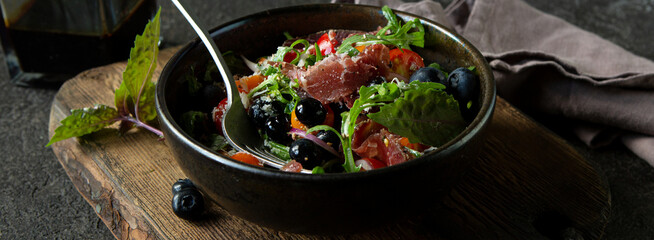 bowl of salad with arugula, bresaola and tomatoes on a dark table