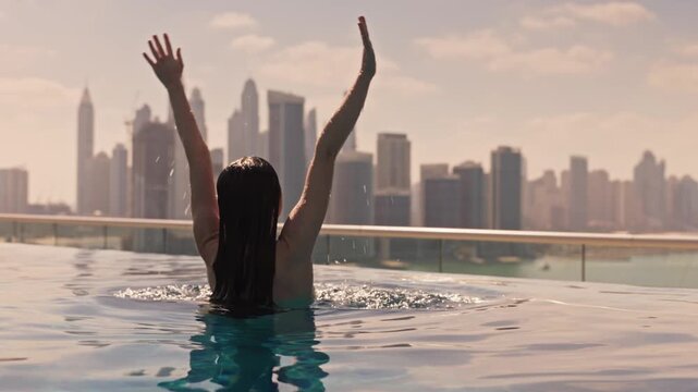 Dubai lifestyle video of a woman in swimwear raising her hands in an infinity pool at sunrise, with Dubai Marina skyline in the background. Lifestyle and vacation concept in Dubai UAE 