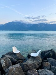 Vevey, Switzerland, view of lake Geneva and the Swiss Alps.  Two chairs set on the rocks to look out into the lake and surrounding landscape.