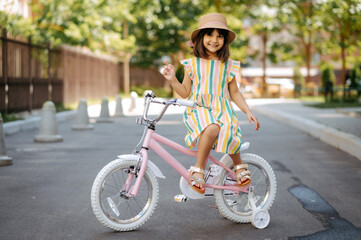 Girl in dress and hat riding a pink bicycle.