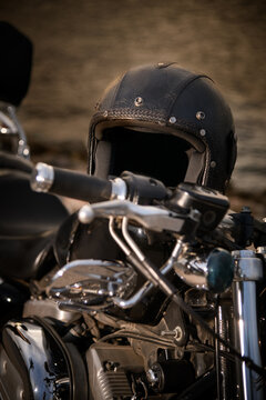 A close-up shot of a leather-clad helmet placed on the seat of a chopper-style motorcycle. The image captures the rugged, classic look of the gear and bike, set against a blurred background