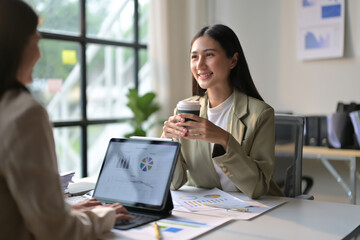 Fototapeta premium Business Meeting in Modern Office with Two Professional Women Discussing Charts and Graphs on Laptop