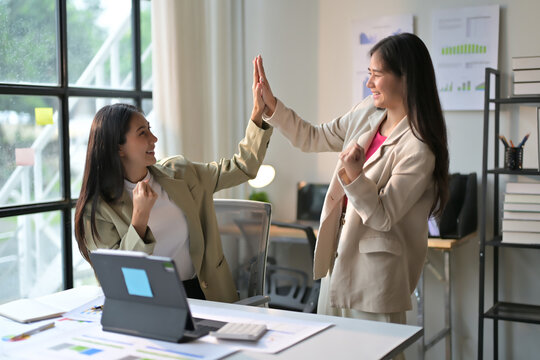 Two Businesswomen Celebrating Success with a High Five in a Modern Office Environment