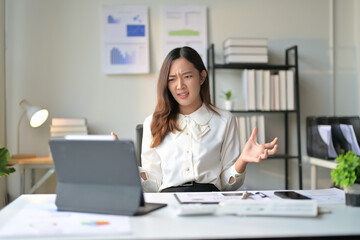 Frustrated Businesswoman at Desk with Laptop in Modern Office, Analyzing Data and Charts on Wall, Experiencing Work Stress