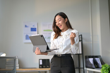 Young Professional Woman Celebrating Success While Working on a Tablet in a Modern Office Environment