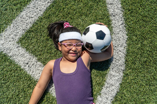 Fototapeta Smiling young girl holding a soccer ball on the field