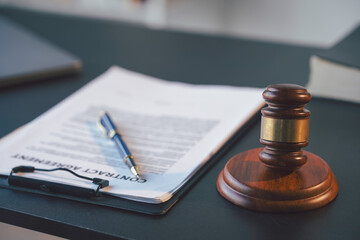 Wooden gavel is sitting on a sound block next to a contract agreement and a pen on a desk