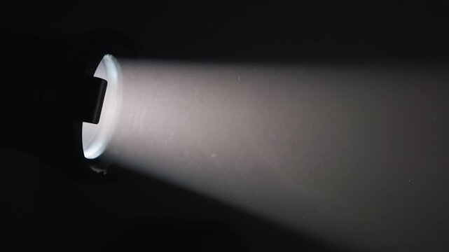 A focused beam of light from a handheld flashlight illuminates a dark room, creating a distinct linear ray across the shadowy space