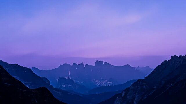 Timelapse of the sun rising over a mountain range, the sky transitioning from dark to light as colors change from deep blues to vibrant oranges and pinks. Dramatic sky, heaven, changing, tranquility