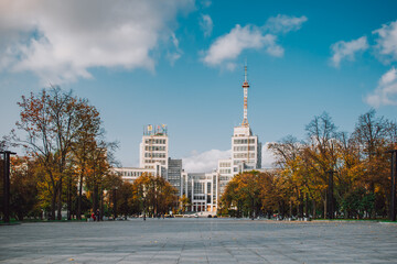 Wide cityscape with modern buildings and autumn trees under a clear blue sky