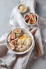 A wholesome bowl of oatmeal topped with fresh figs and sliced almonds, set on a rustic linen cloth. Accompanying small bowls of figs and almonds enhance the cozy breakfast scene