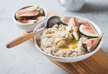 A wholesome bowl of oatmeal topped with fresh figs and sliced almonds, set on a rustic linen cloth. Accompanying small bowls of figs and almonds enhance the cozy breakfast scene