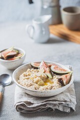 A wholesome bowl of oatmeal topped with fresh figs and sliced almonds, set on a rustic linen cloth. Accompanying small bowls of figs and almonds enhance the cozy breakfast scene