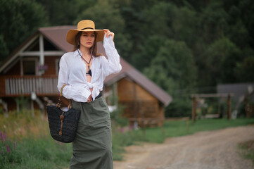 Fashionable confident woman wearing trendy summer hat, white linen shirt, green skirt, holding black wicker  straw bag, walking outdoor.  Fashion portrait. Copy, empty, blank space for text
