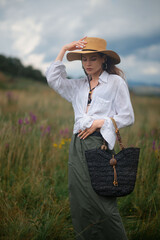 Fashionable confident woman wearing trendy summer outfit with wide brim hat, white linen shirt,...